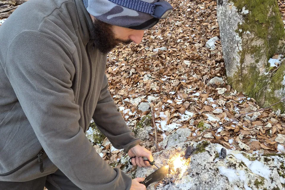 Allumage d’un feu au briquet-silex sur un rocher enneigé, en forêt